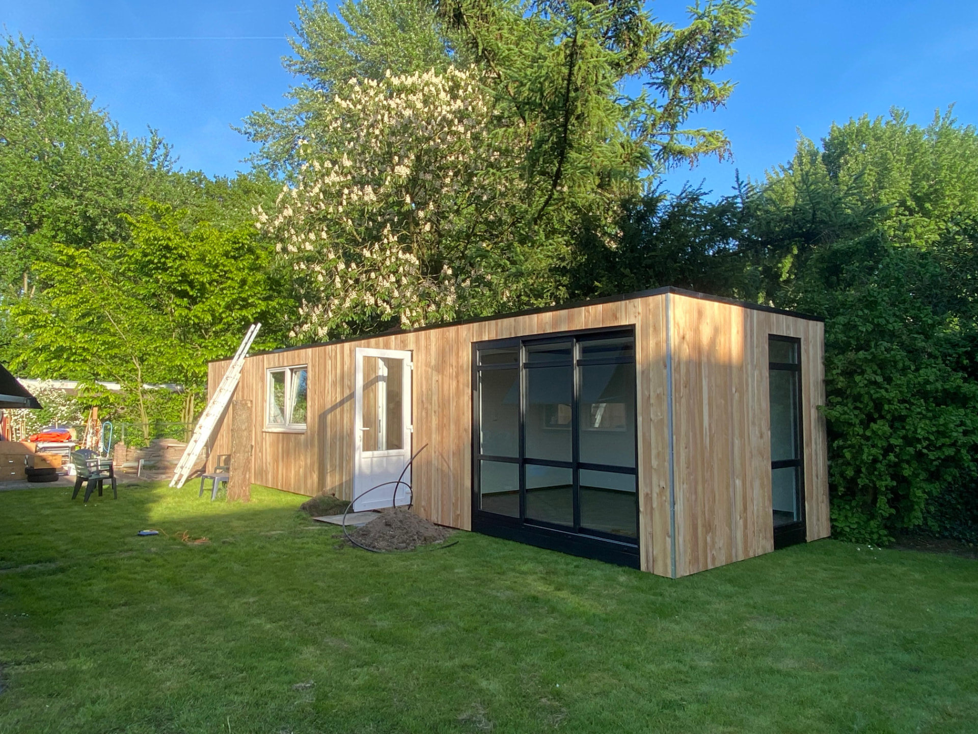 Houten tuinhuis unit met aluminium kozijnen in een groene tuin