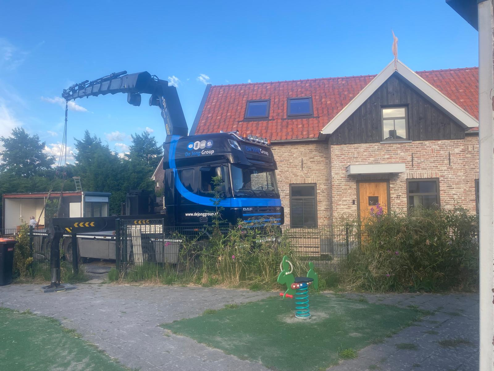 Vrachtwagen met laadkraan van De Jong Group tijdens hijswerk bij een woning
