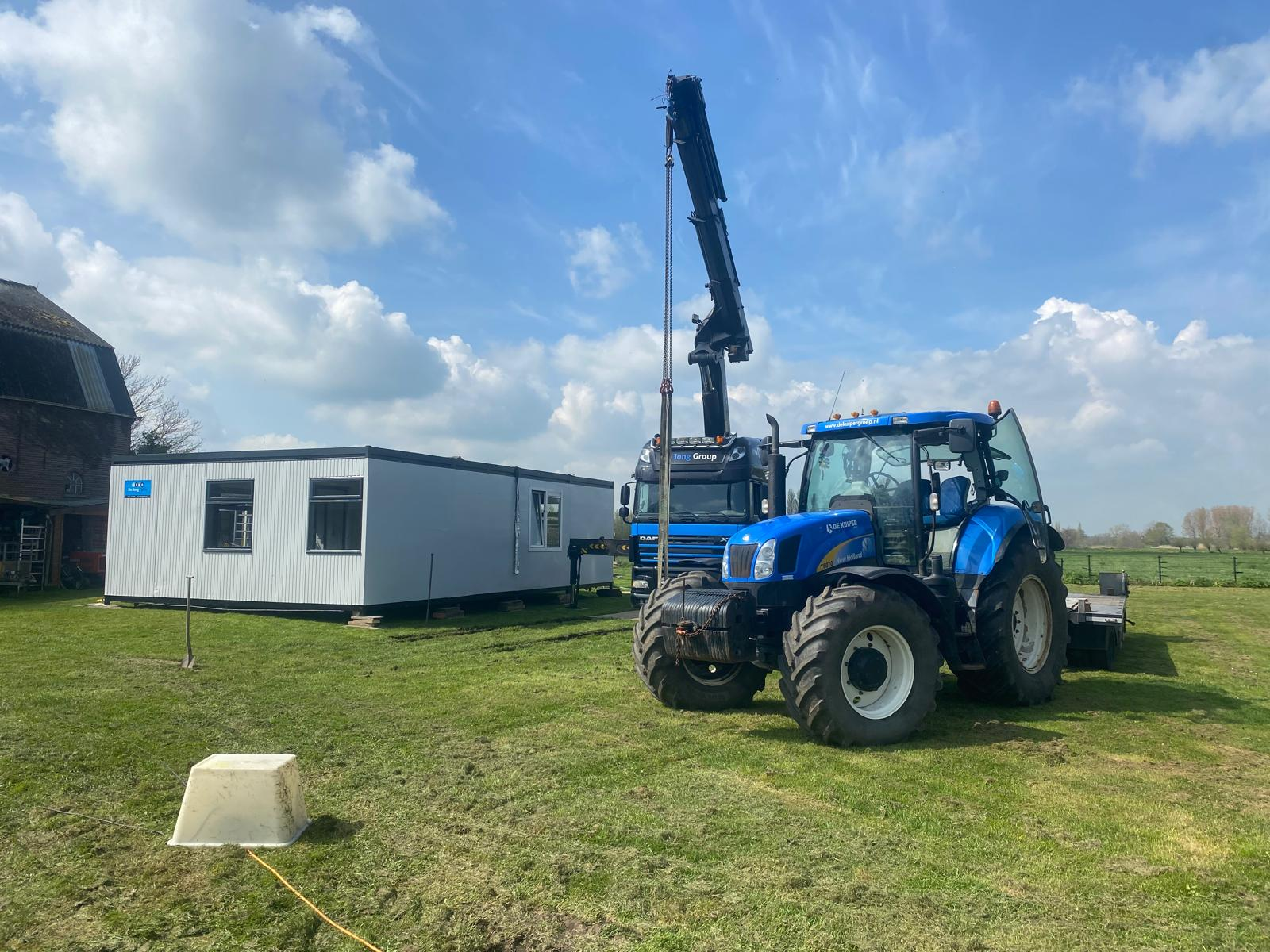 Vrachtwagen met laadkraan en tractor met dieplader bij het plaatsen van een unit in een weiland